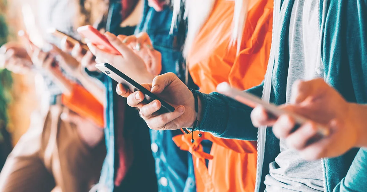 Multiple hands hold smartphones, people engrossed in their screens, suggesting digital interaction or media consumption in a group.